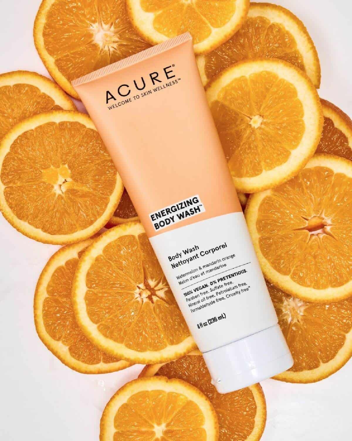 A tube of Acure Beauty body wash in orange and white against a background of orange slices. 