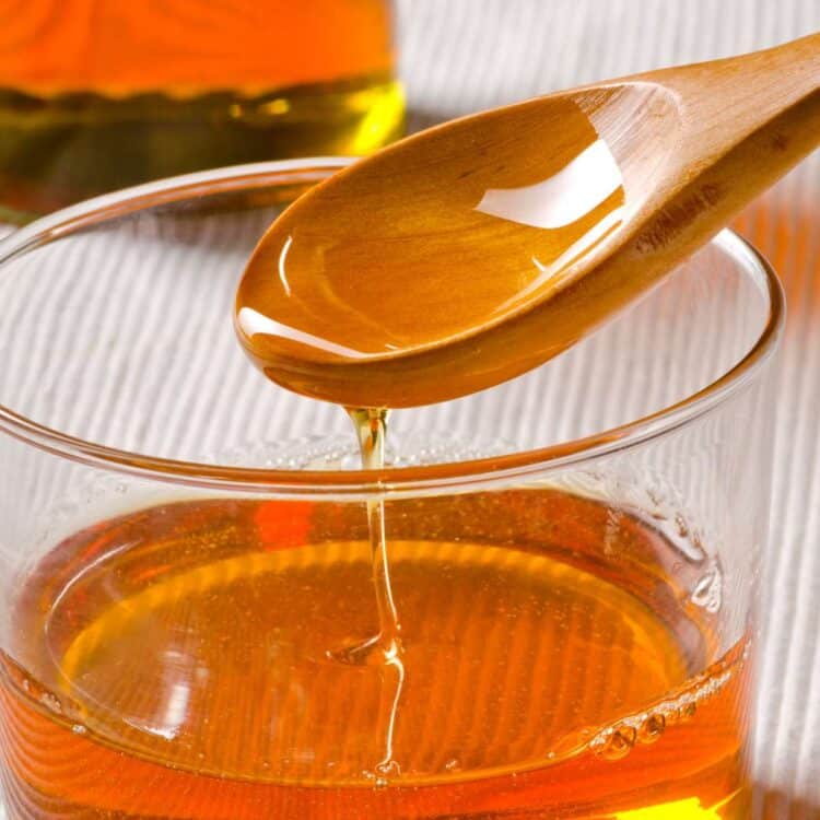 A wooden spoon with some agave nectar dripping off of it into a glass.