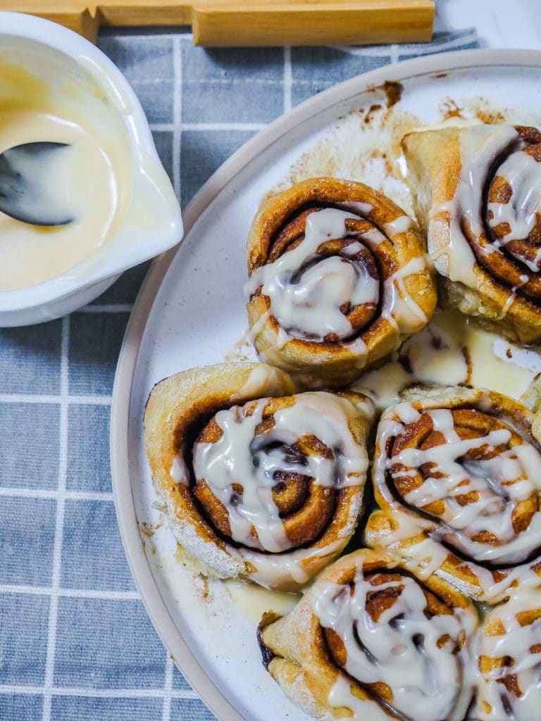 cinnamon rolls on a plate with a pitcher of frosting in the upper left hand corner