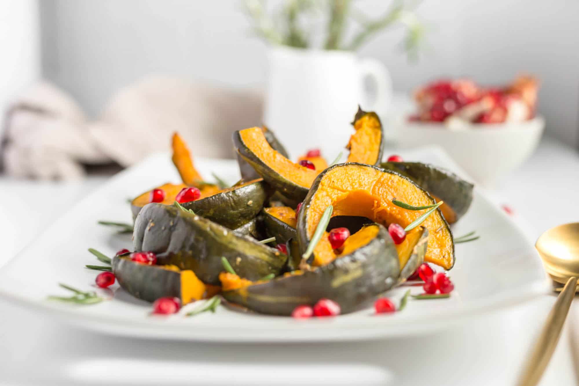 cooked and sliced kabocha squash garnished with pomegranate seeds and rosemary on a white plate