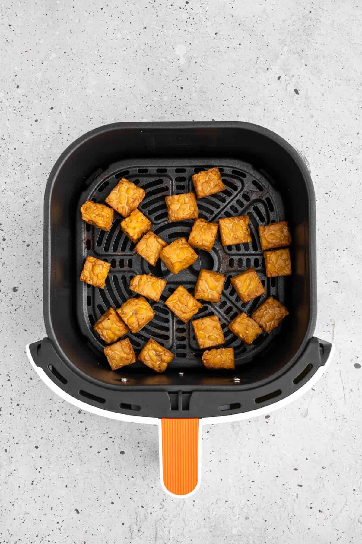 Cooked tempeh in an air fryer basket.