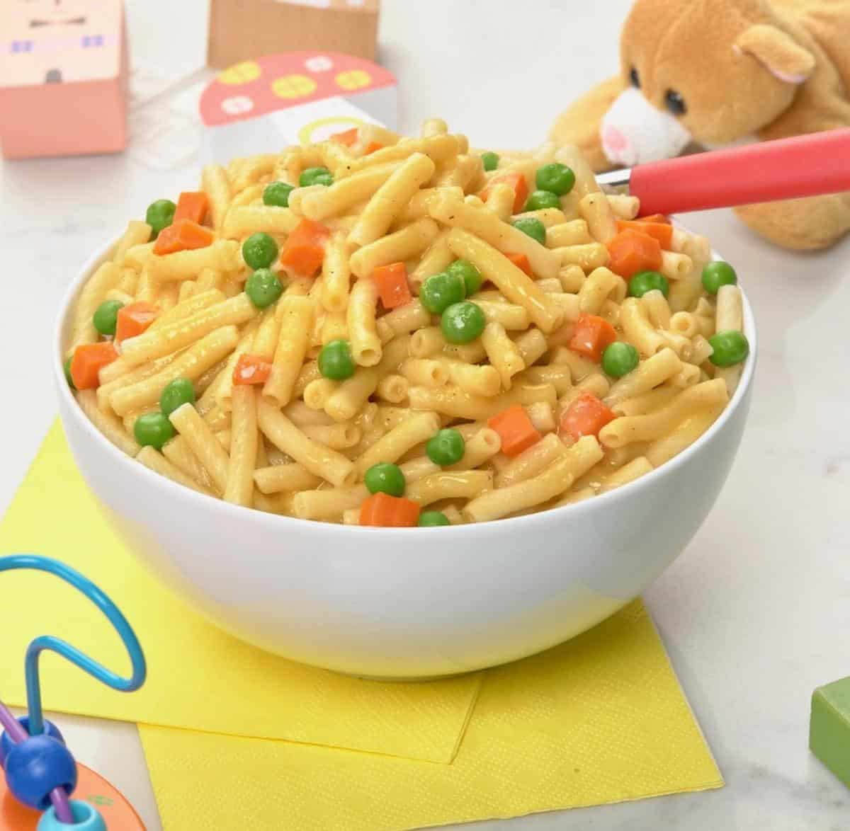 Bowl of vegan mac and cheese with peas and carrots.