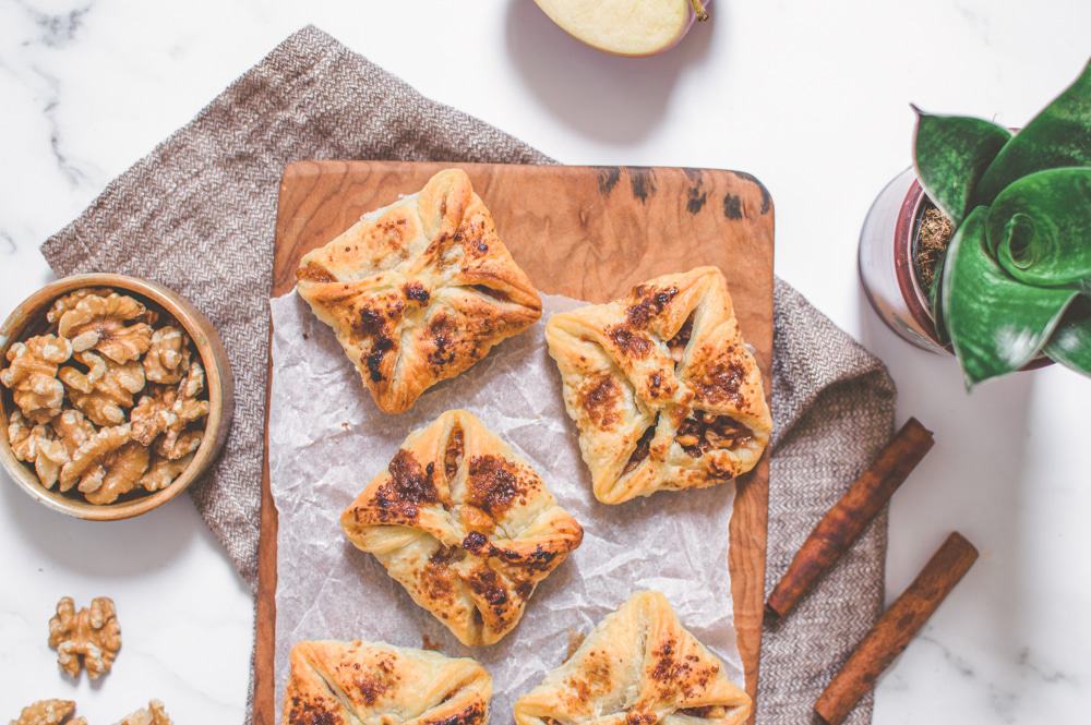 Apple pie pockets on a serving board, surrounded by walnuts and cinnamon sticks.