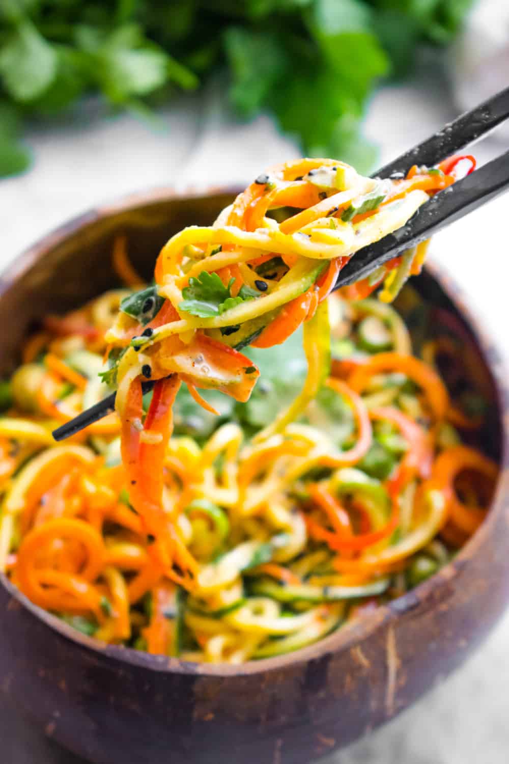 Chopsticks holding up zucchini noodles from a bowl of Asian zucchini noodles.