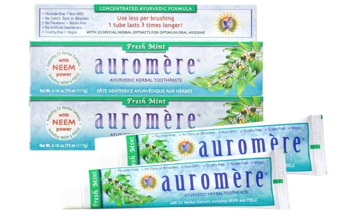 Two tubes of Auromere toothpaste in blueish green tubes laying in front of 2 stacked boxes of Auromere. 