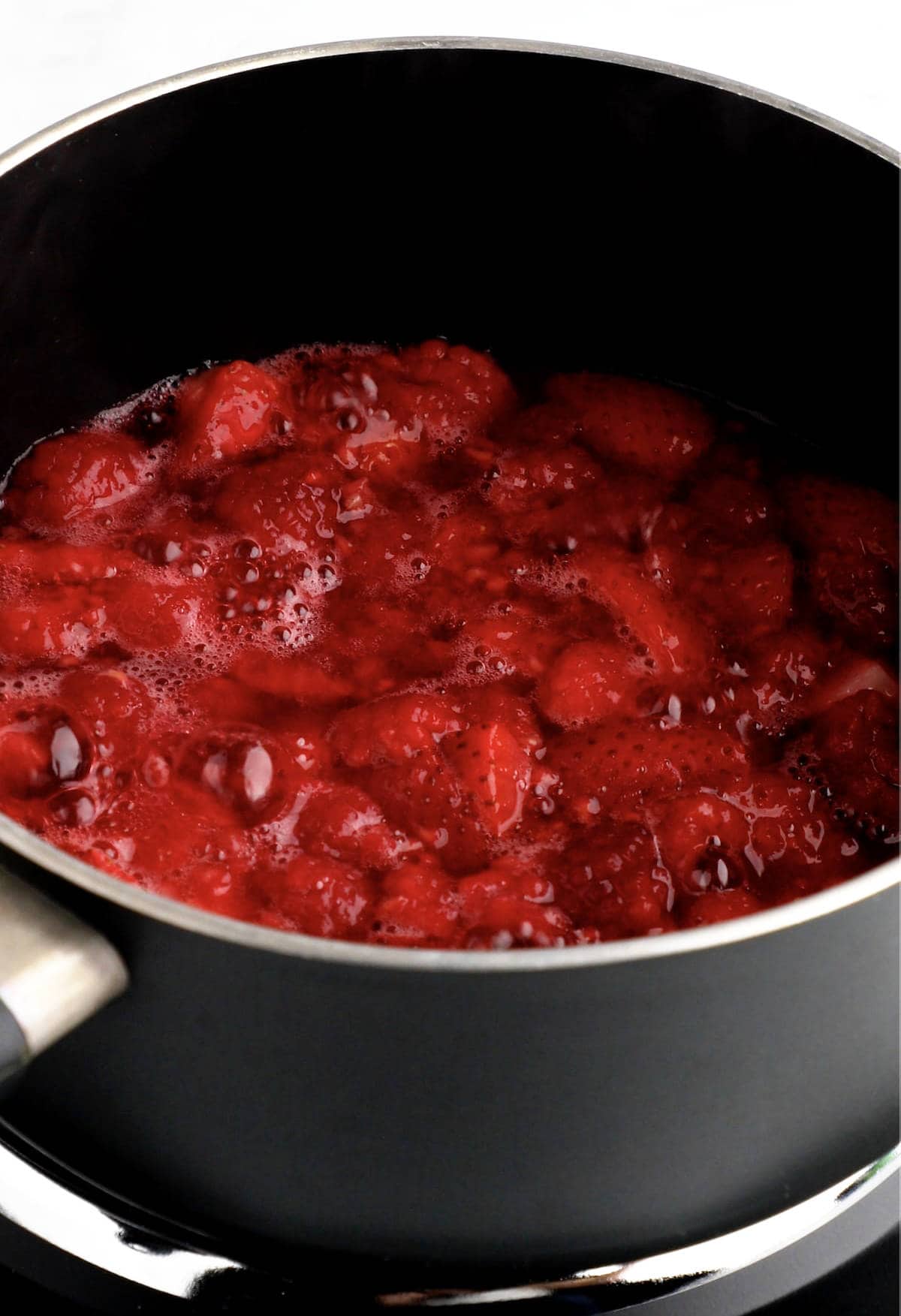 Berry compote cooking in a small sauce pan.