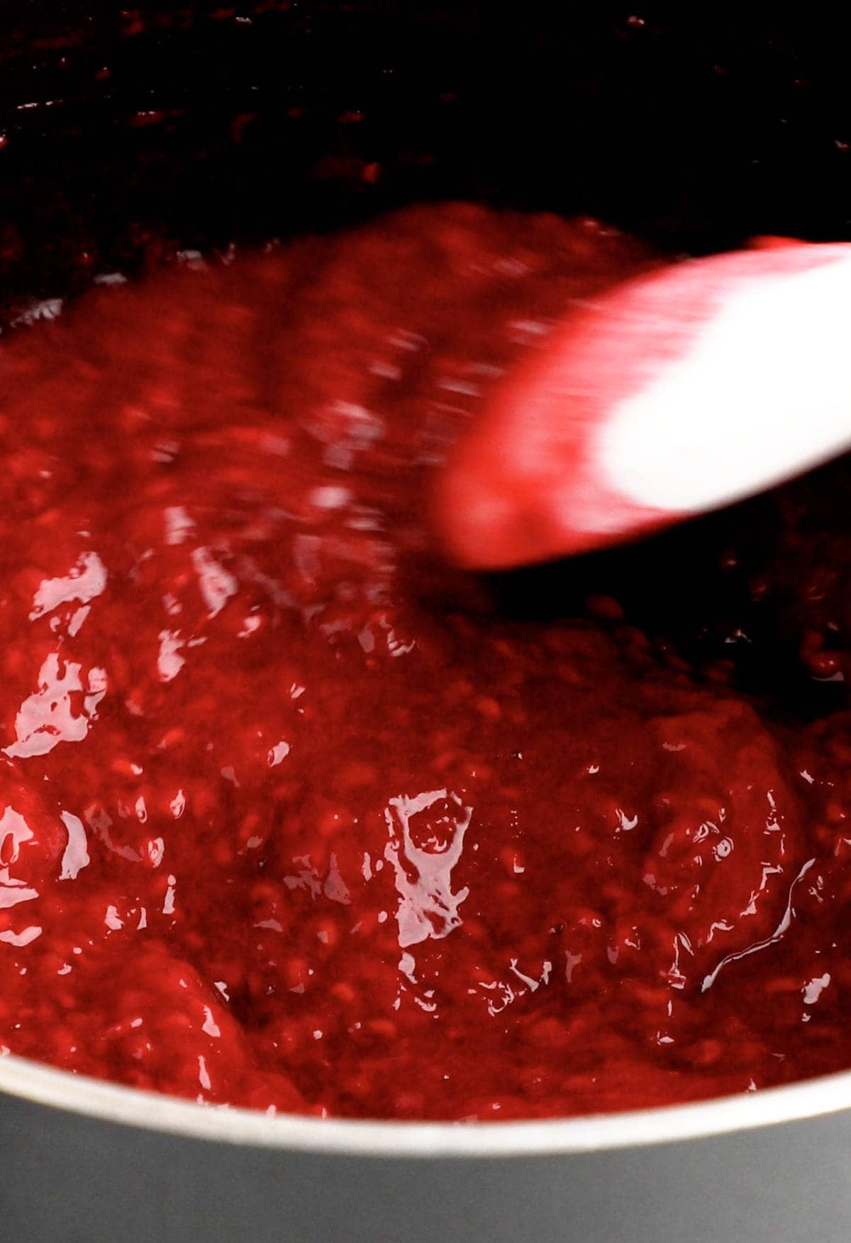 Up close of berry compote in saucepan with a spoon stirring it around.