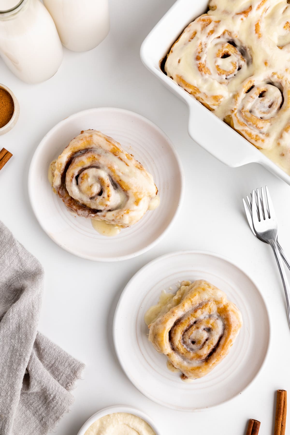 Two vegan cinnamon rolls on plates, covered in frosting.