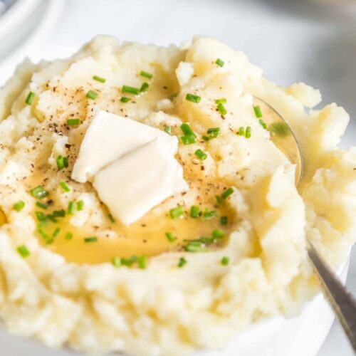 Dairy-free mashed potatoes in a bowl with serving spoon and topped with vegan butter.