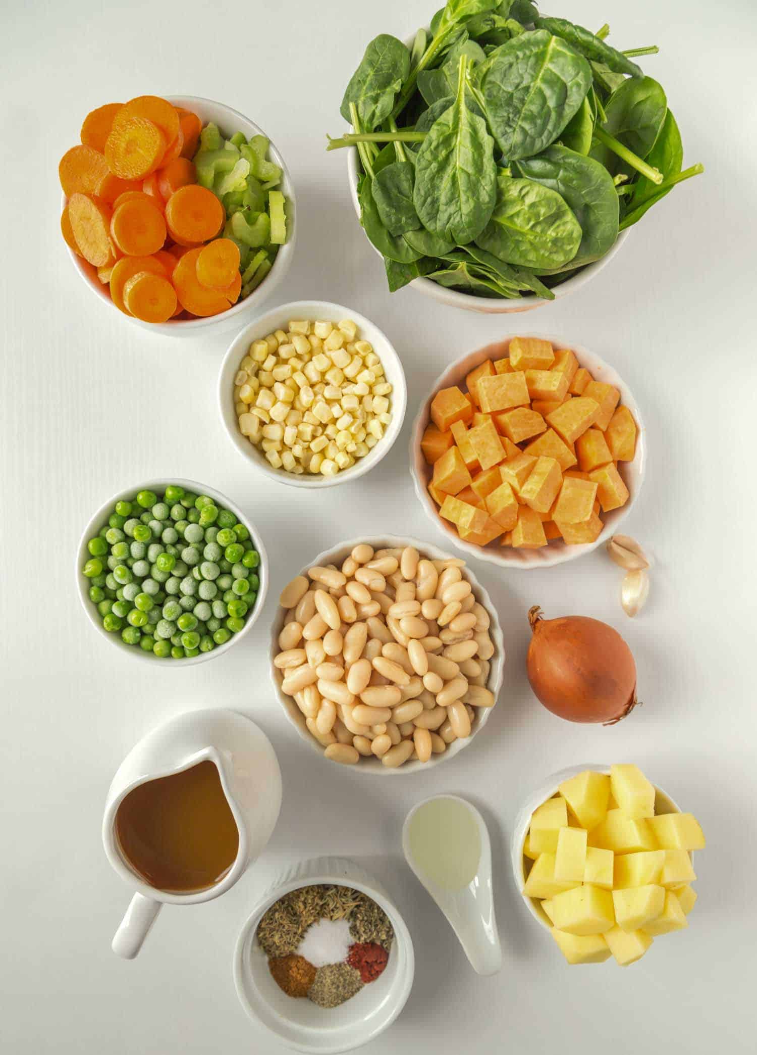 vegan stew ingredients flatlay photo with spinach potato peas veggie broth beans sweet potato and spices