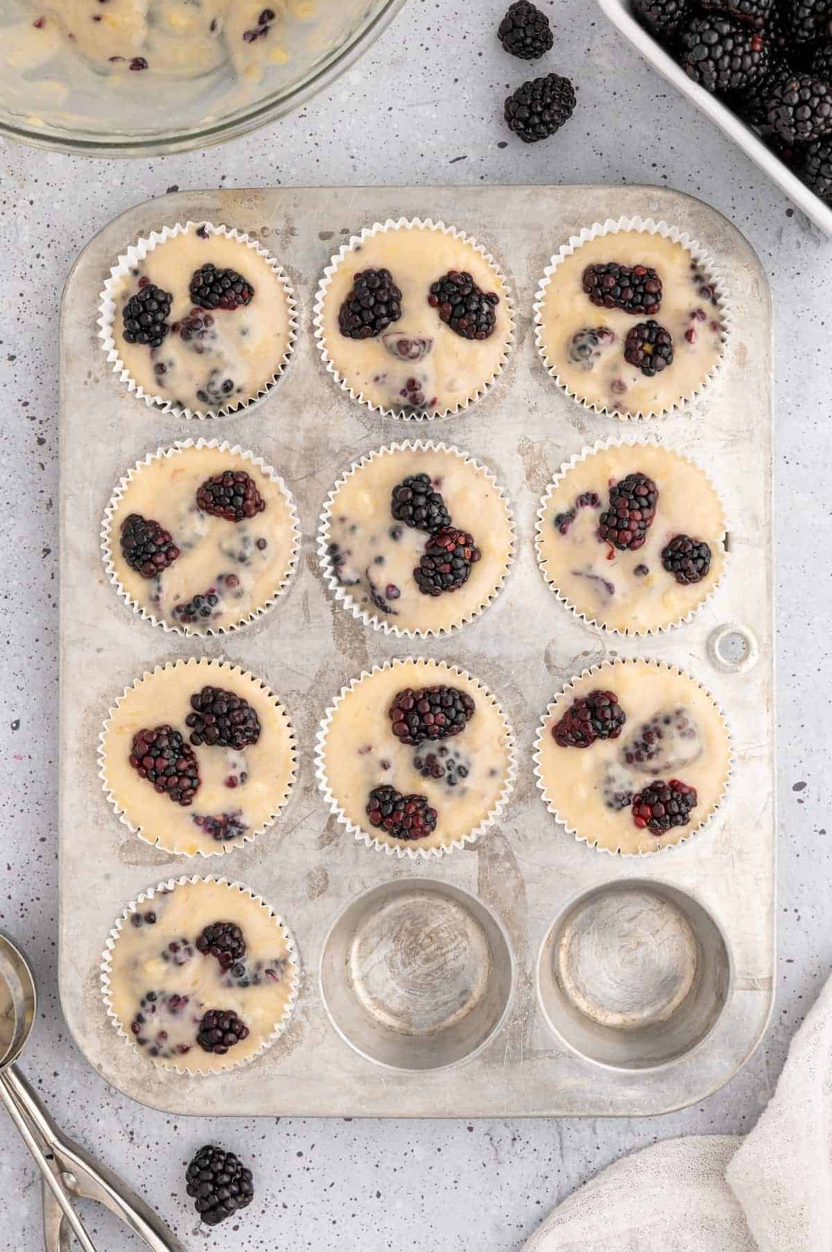 Blackberry muffin batter in a muffin tin topped with fresh raspberries.