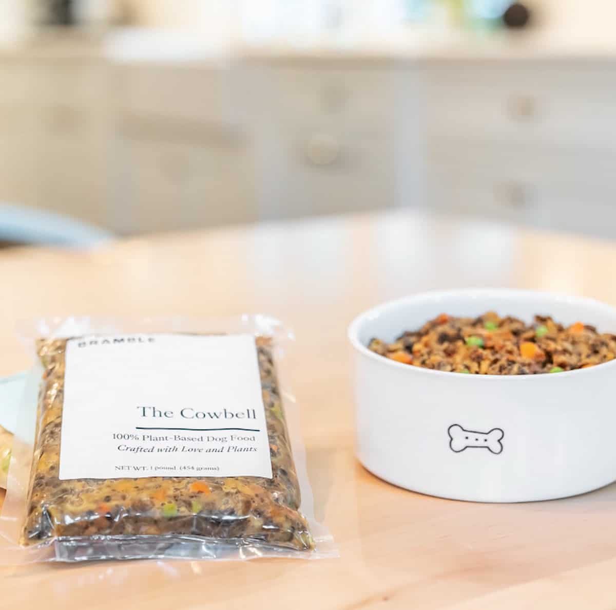 A bowl of vegan dog food next to a package of Bramble The Cowbell 100% Plant-Based Dog Food.