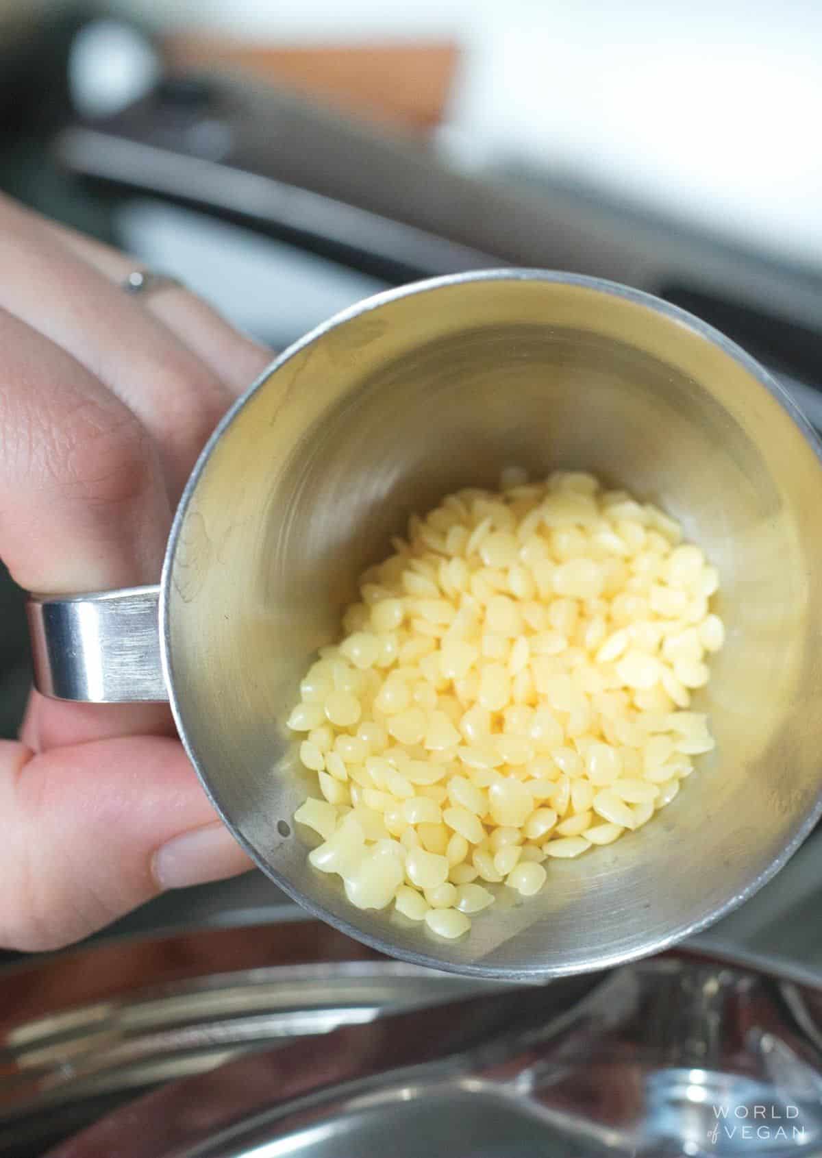 Hand holding a melting mug filled with candelilla wax.