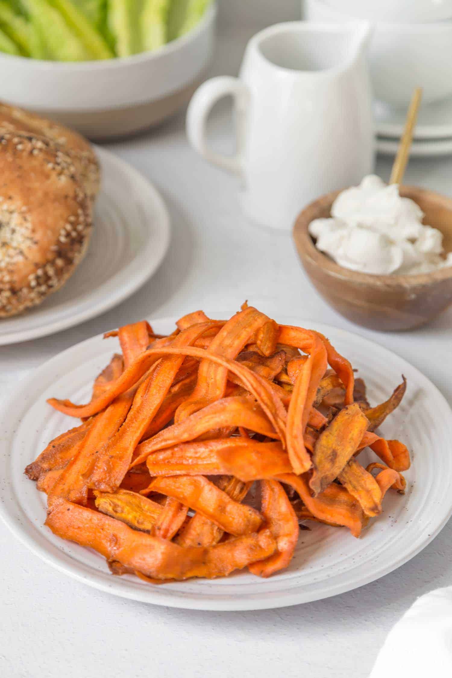 smoky vegan carrot bacon piled up on a white plate next to brunch bagels and vegan sour cream