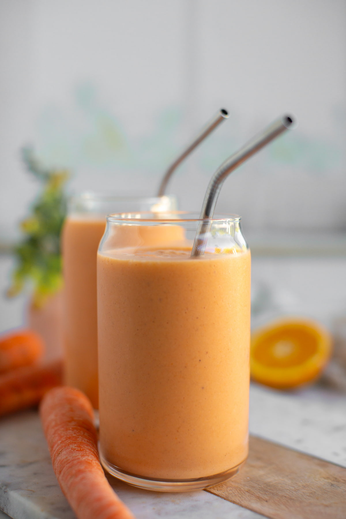 Two glasses of carrot banana smoothie next to a carrot.
