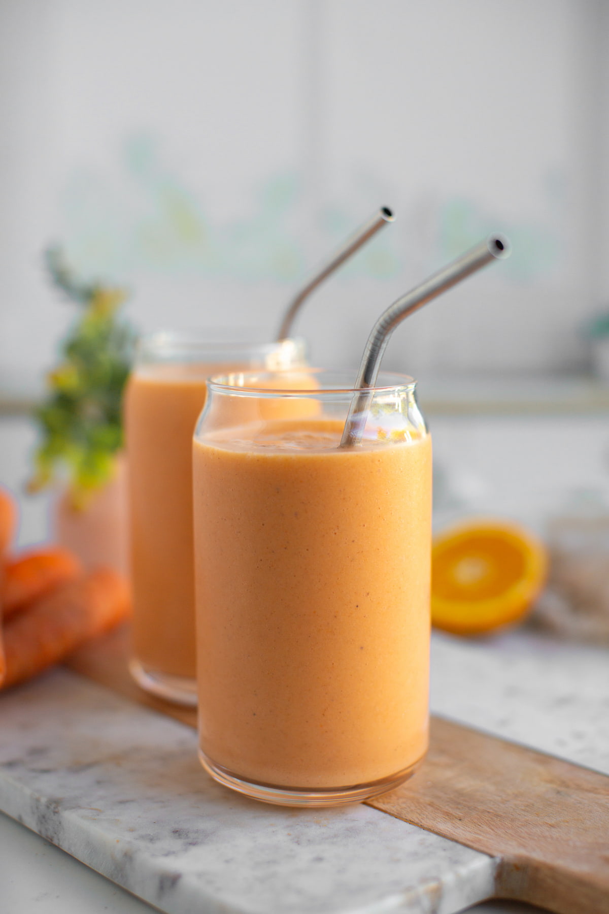 Carrot smoothies in glass cups with metal straws.