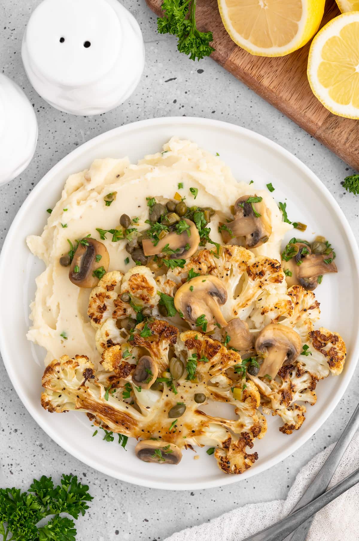 Cauliflower steaks served on a plate with mashed potatoes and piccata sauce.