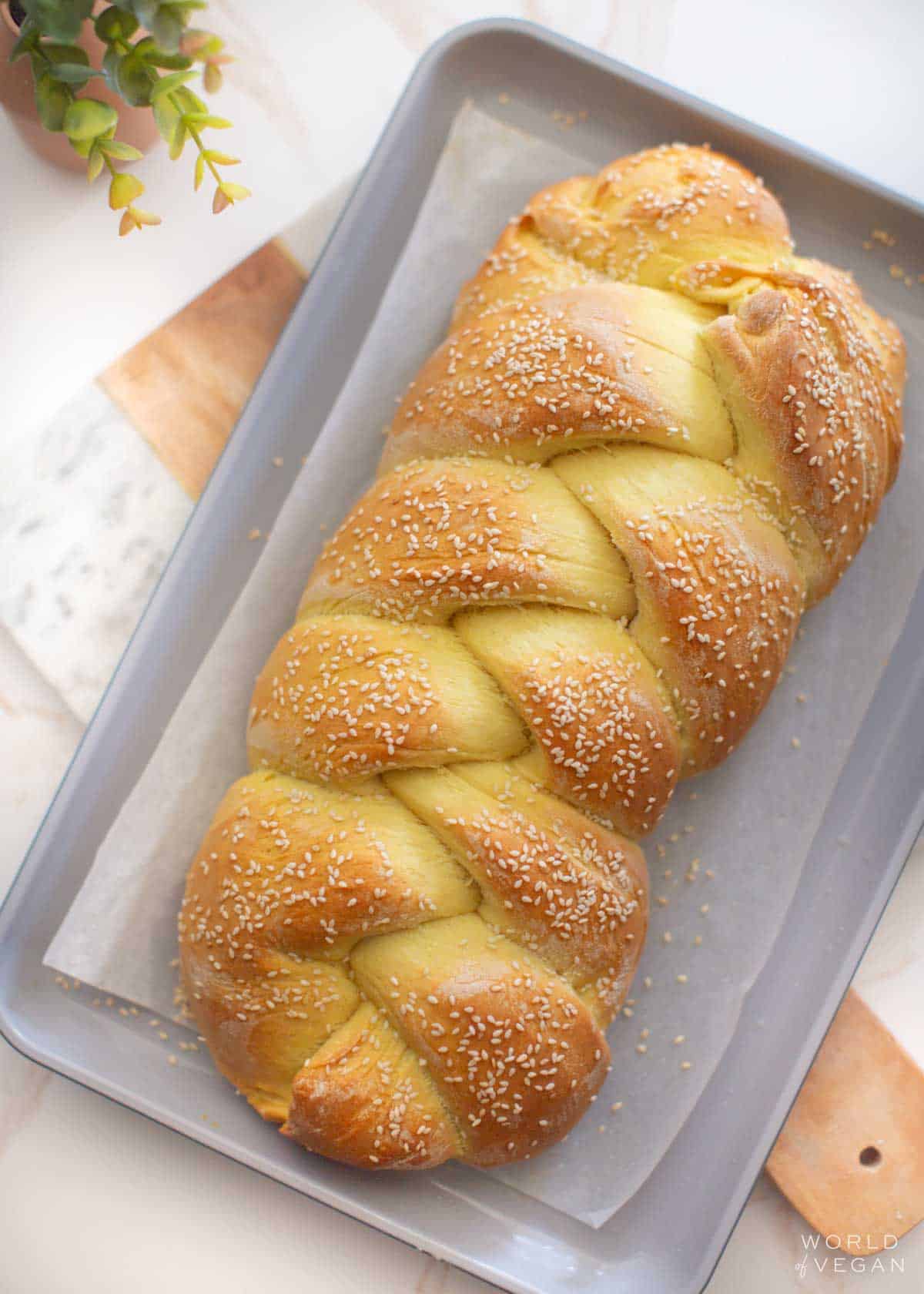 Three-strand braided vegan challah on a baking tray.