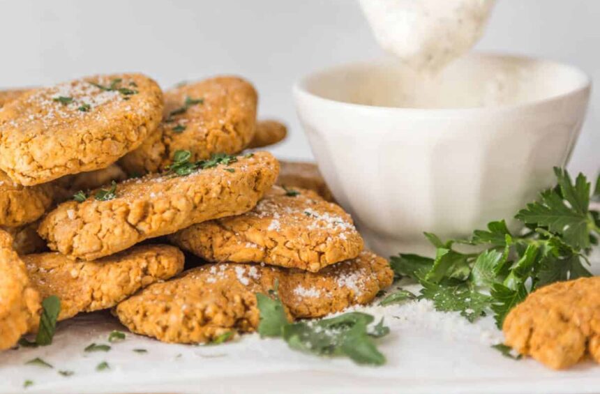 Pile of chickpea nuggets next to a bowl of vegan mayo ranch dip with a dipped nugget hovering over the bowl.