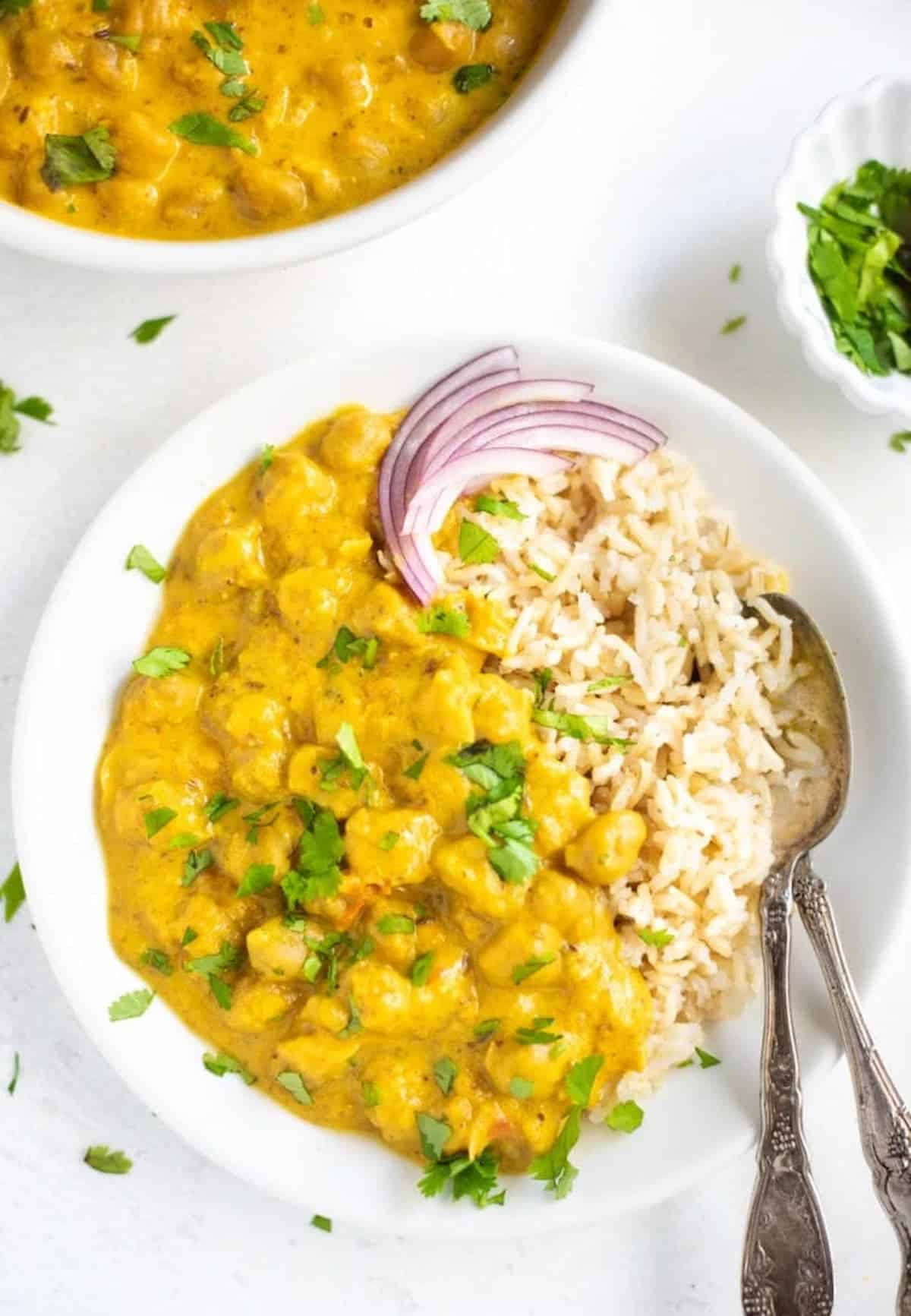 Bowl of chickpea curry and rice with slices of red onion and cilantro on top.