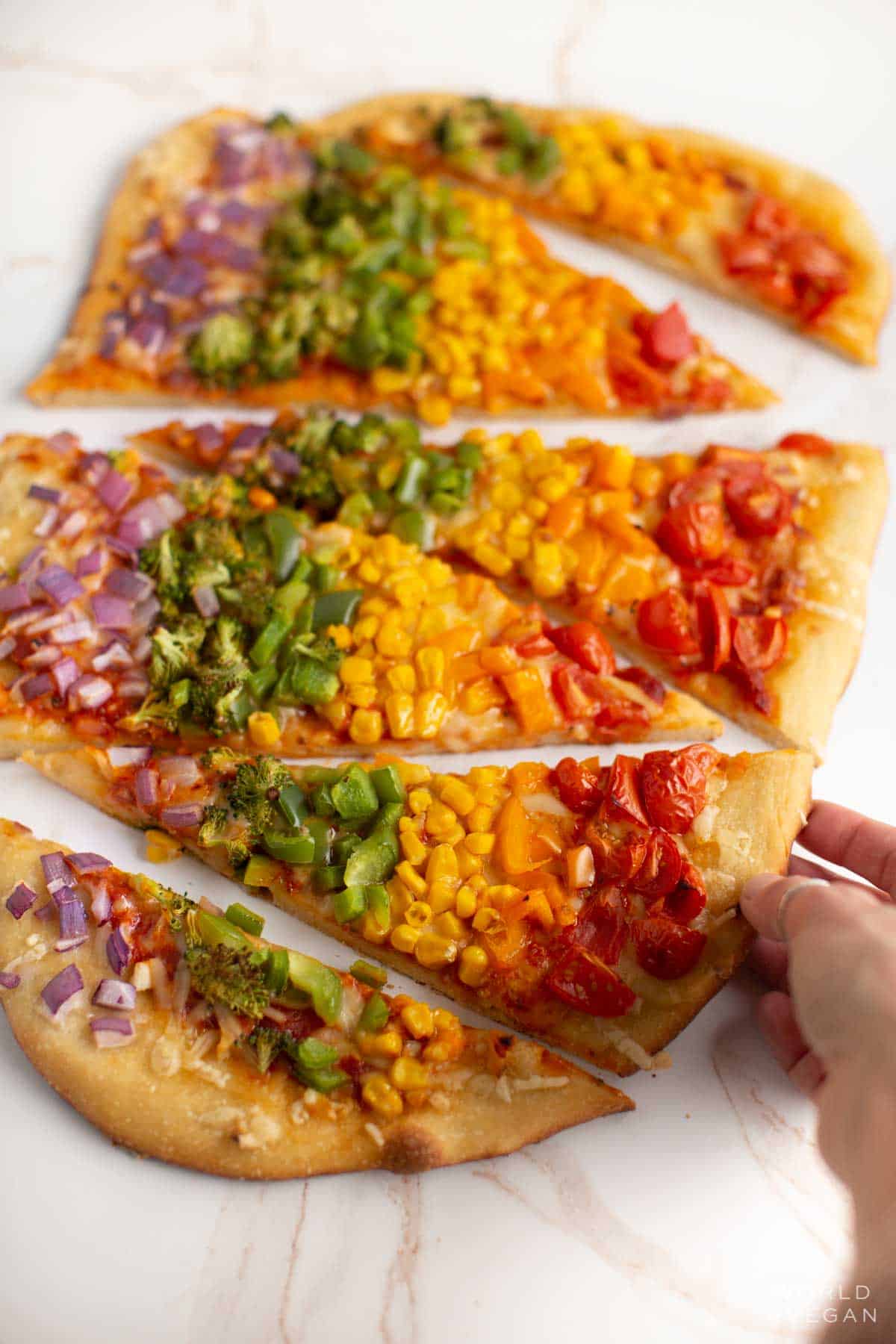 Homemade rainbow pizza with red, orange, yellow, green, and purple veggies cut into slices.