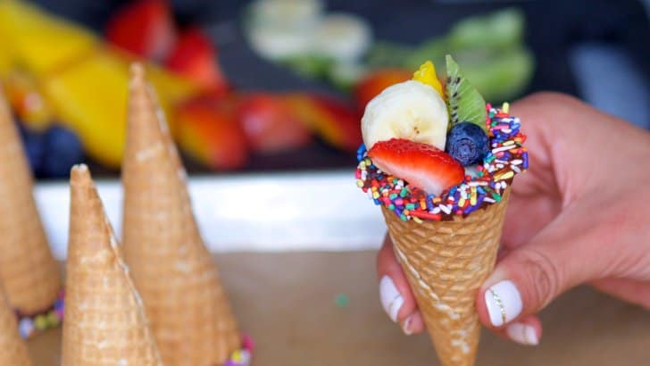 hand holding a chocolate-dipped cone with chocolate and sprinkles holding different fruits in it
