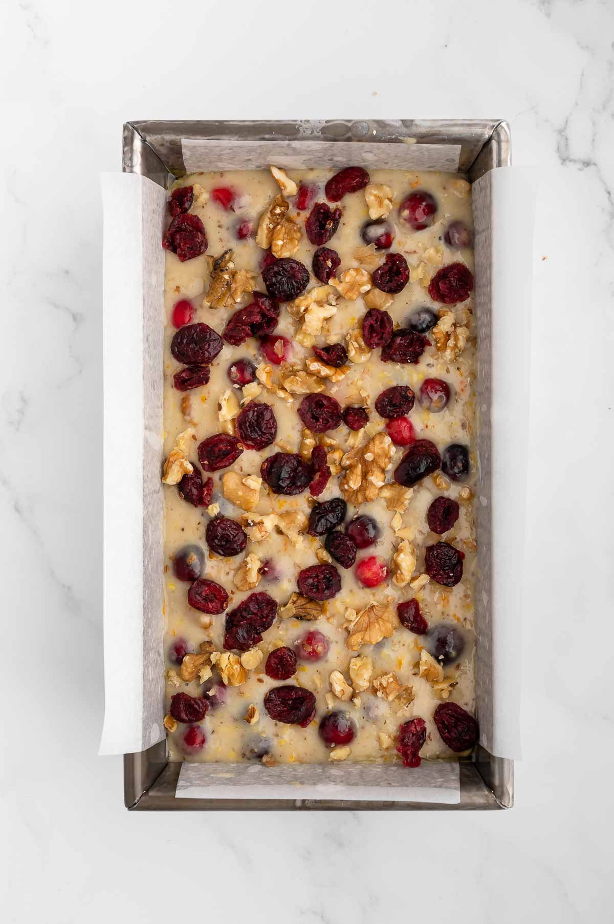 Walnut cranberry bread batter in a loaf pan, topped with fruit.