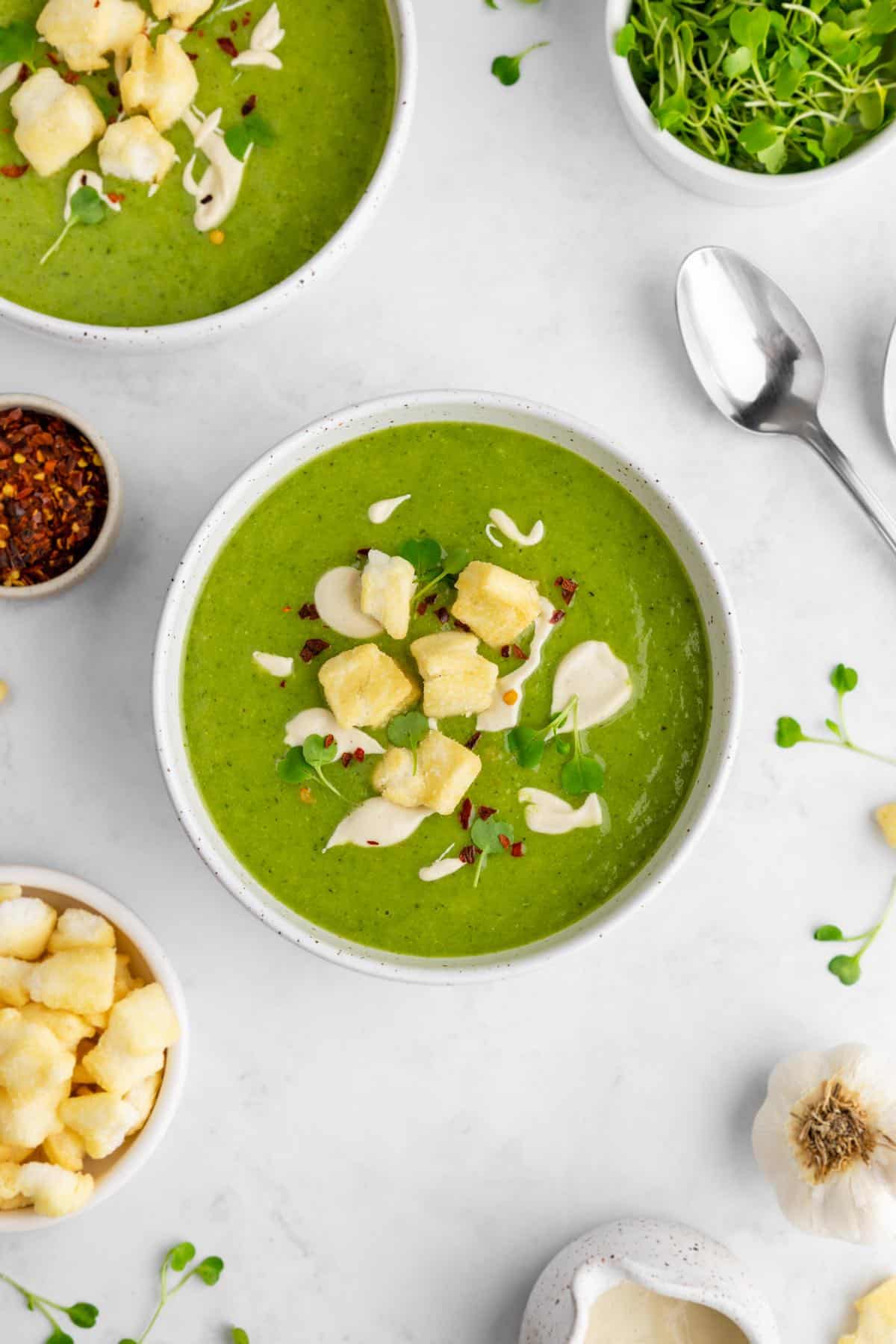 Bright green pea soup served in bowls topped with mochi croutons and a cashew cream drizzle.