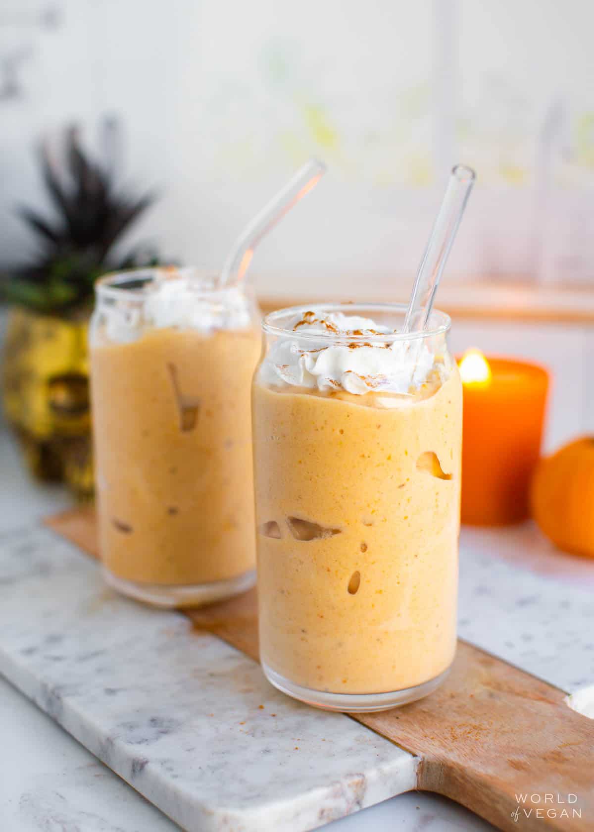 Two glasses of pumpkin milkshake served with glass straws and vegan whipped cream.