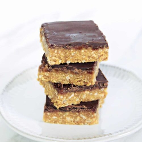 Crispy Caramel Squares stacked on a plate topped with chocolate.