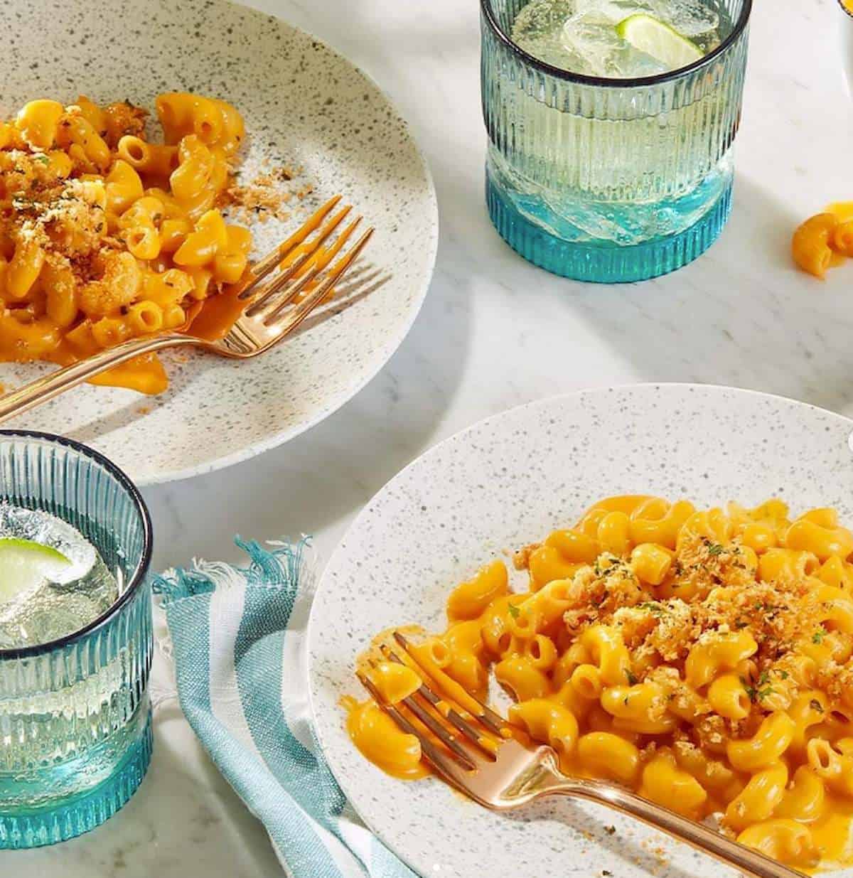 Two plates of vegan cheezy mac with forks, and topped with breadcrumbs.