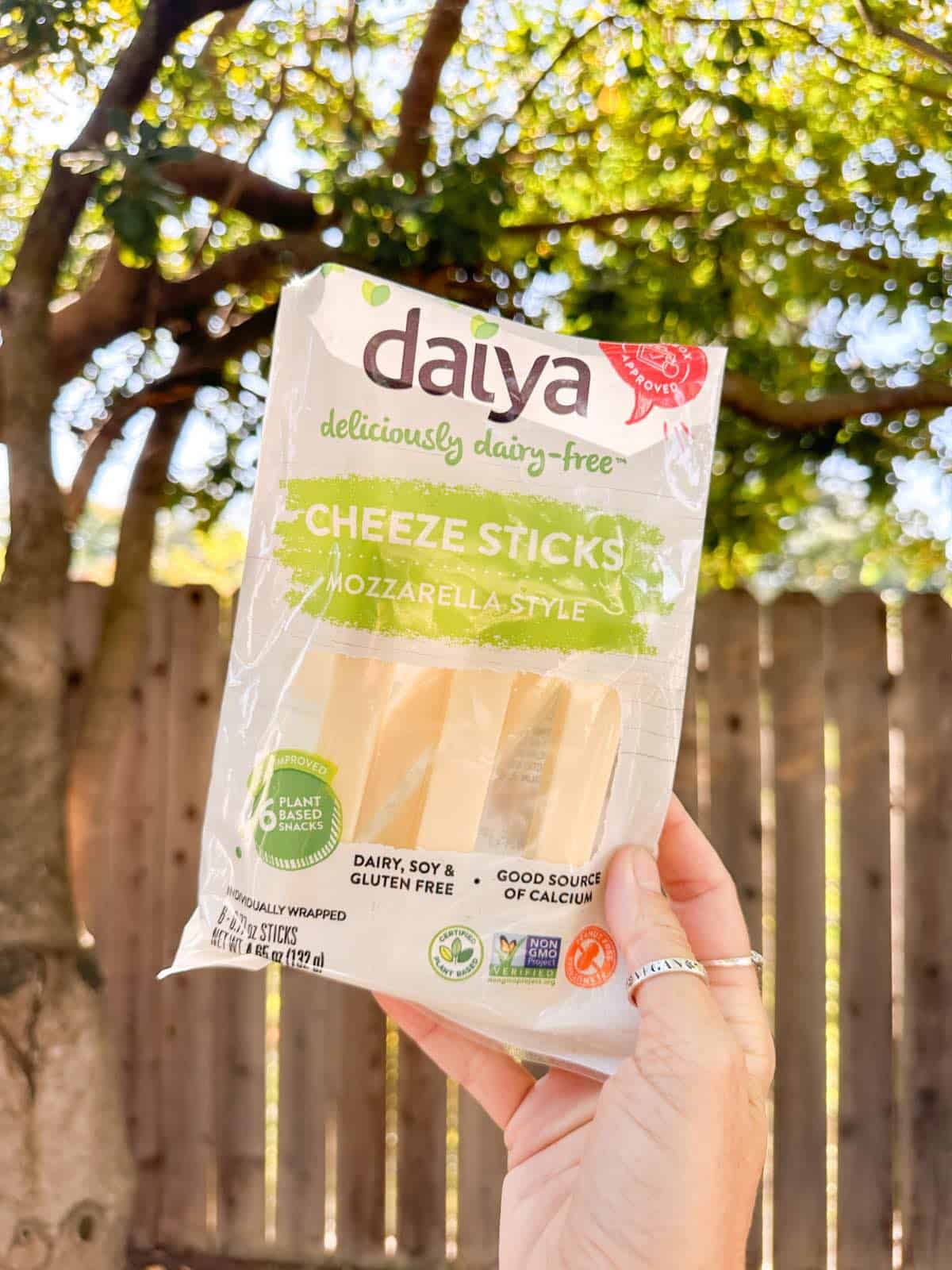 Woman holding up a package of Daiya's vegan mozzarella cheese sticks. 