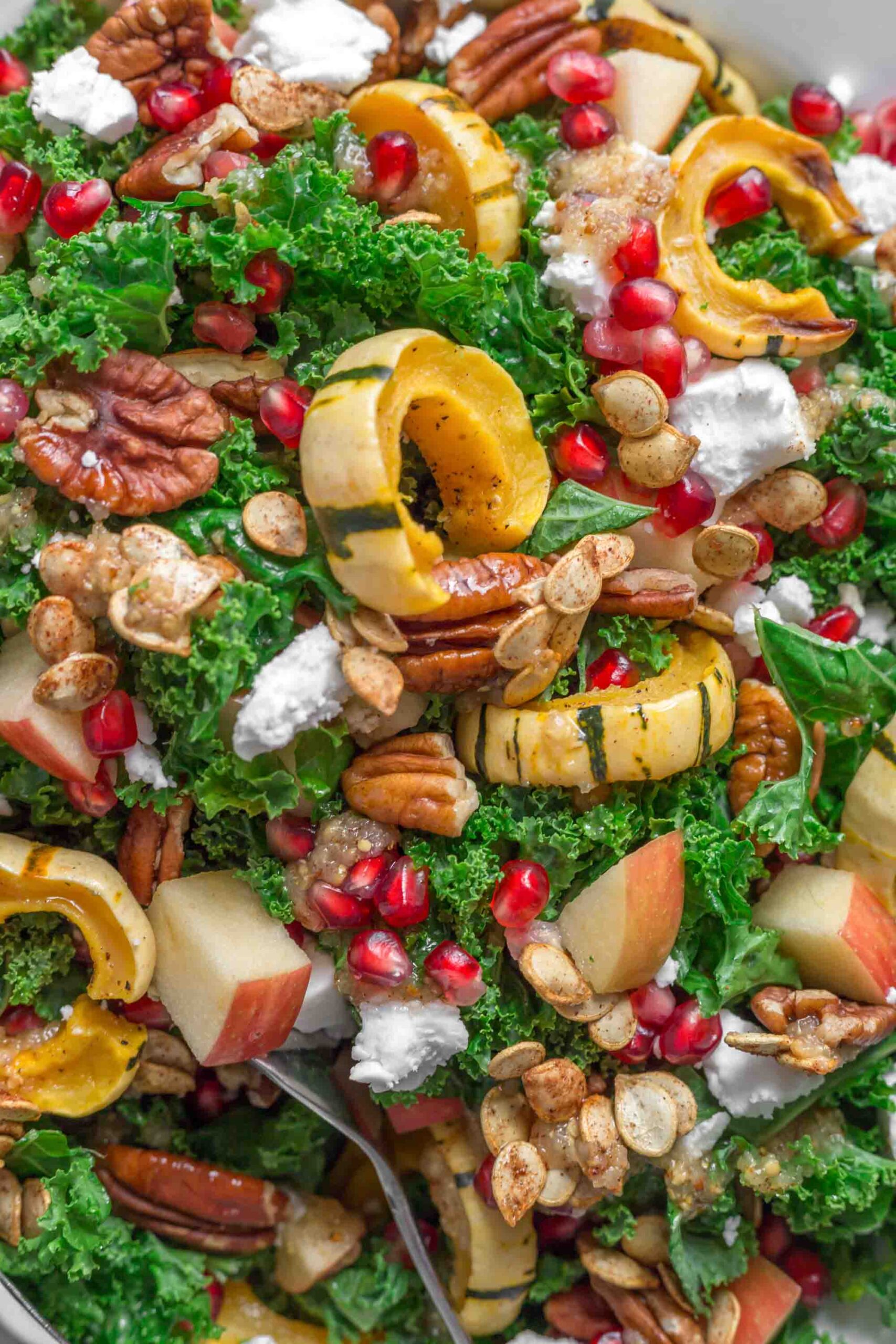 A delicata squash kale salad holiday dish with vibrant green kale and pomegranate seeds.