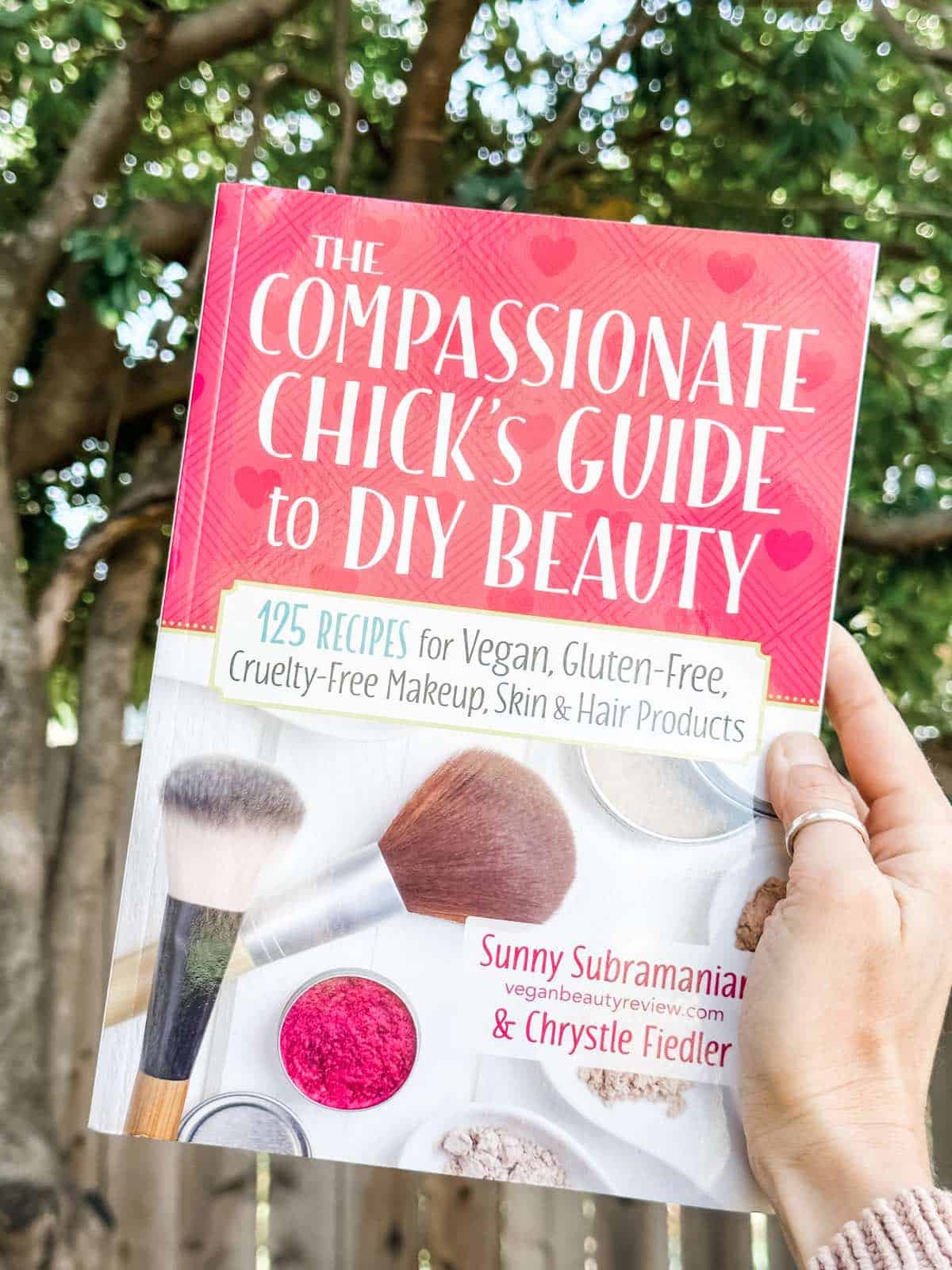 Holding out a copy of the vegan beauty book The Compassionate Chick's Guide to DIY Beauty by Sunny Subramanian. 