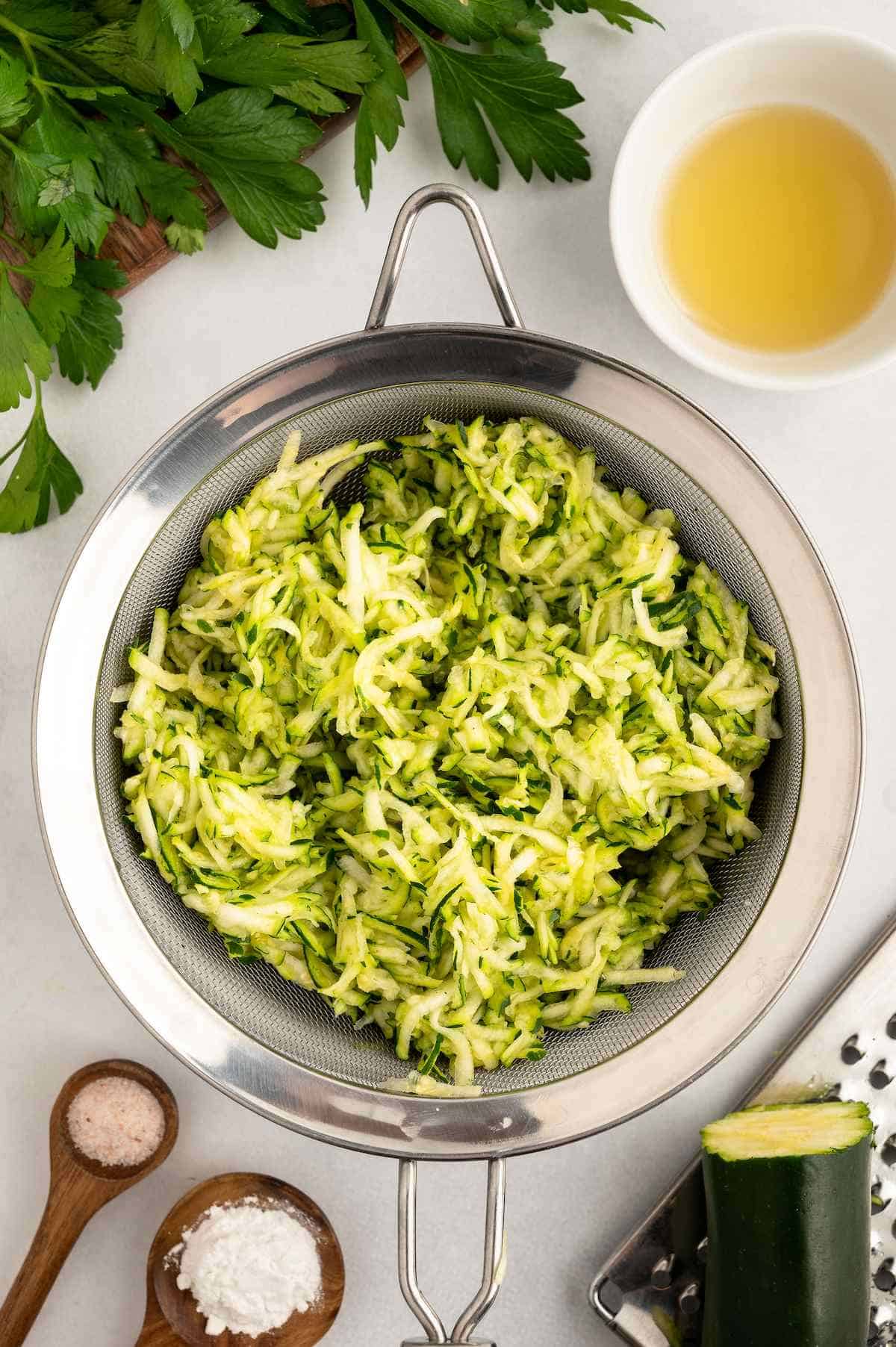Grated zucchini in a mesh strainer.