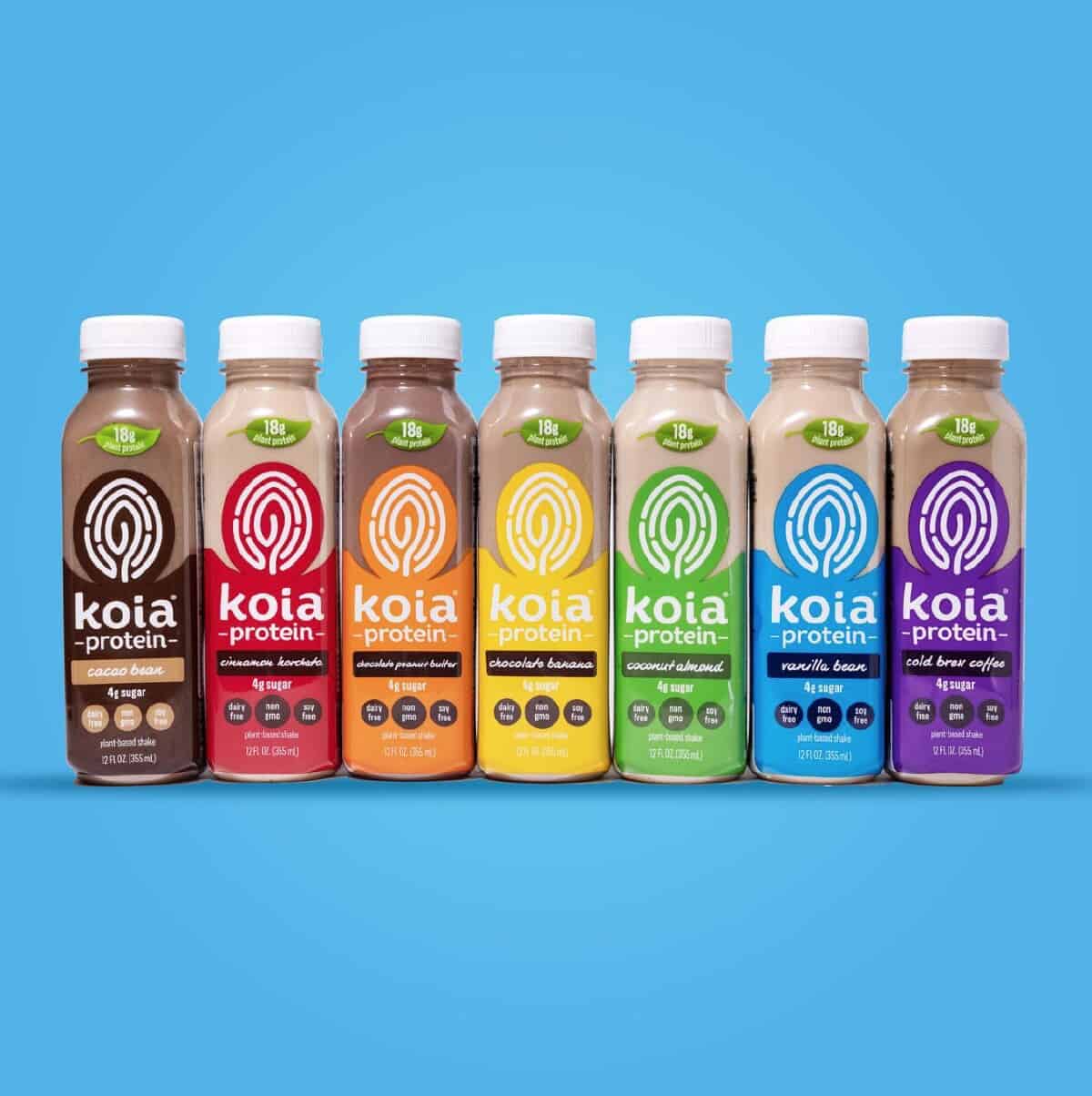 A line of seven rainbow colored Koia plant-based protein shakes against a light blue background.