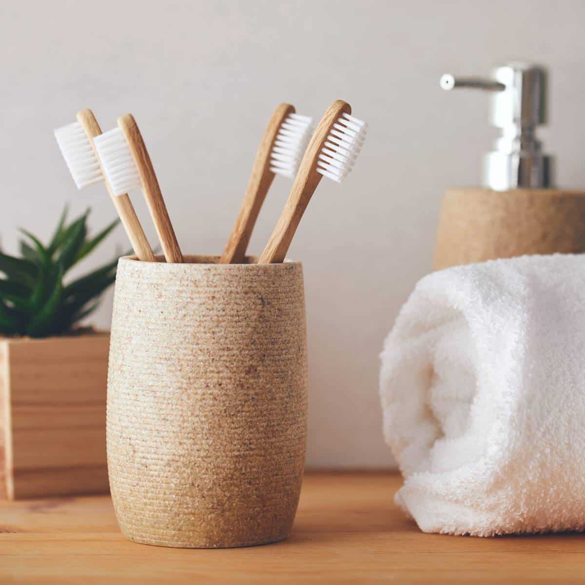 Bathroom cup with earth conscious toothbrushes and vegan toothpaste surrounded by bathroom accessories. 