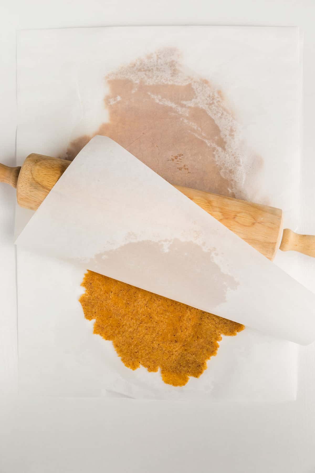 Almond flour dough rolled between two pieces of parchment paper with a rolling pin.