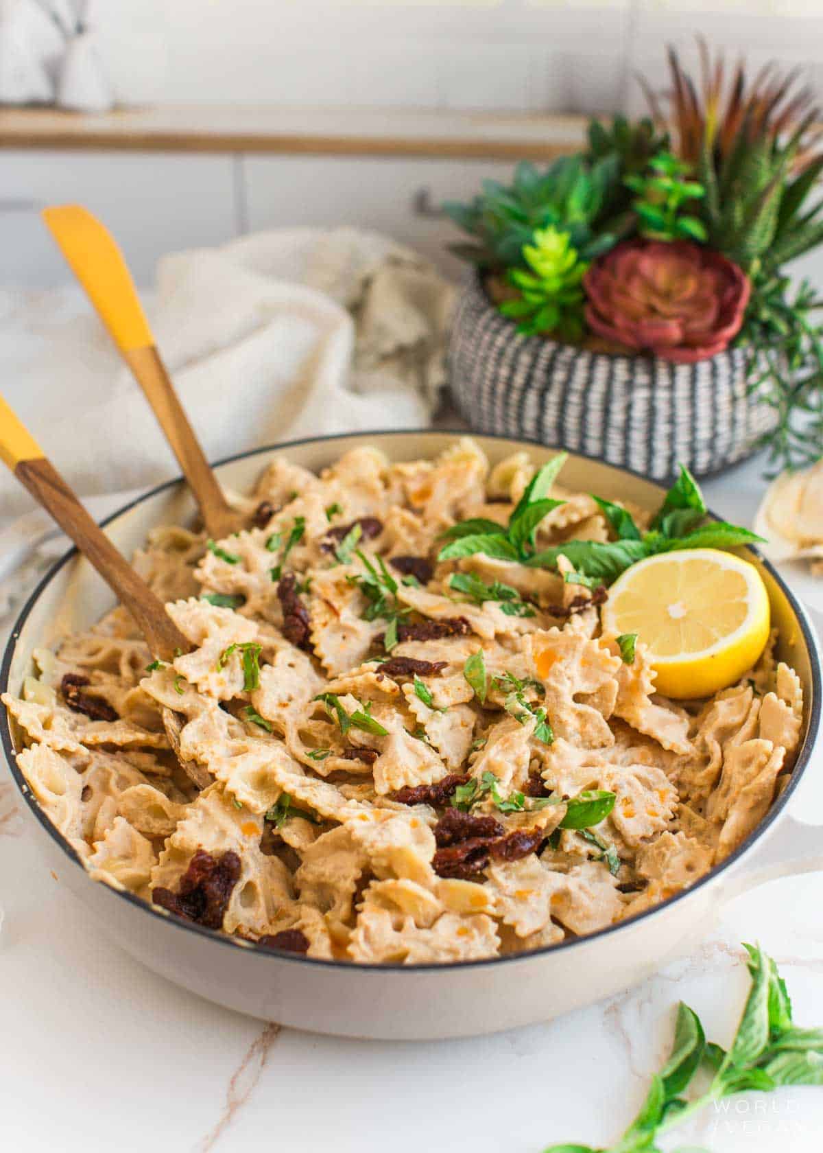 Sun-dried tomato sauce pasta in a pan with serving utensils and half a lemon.