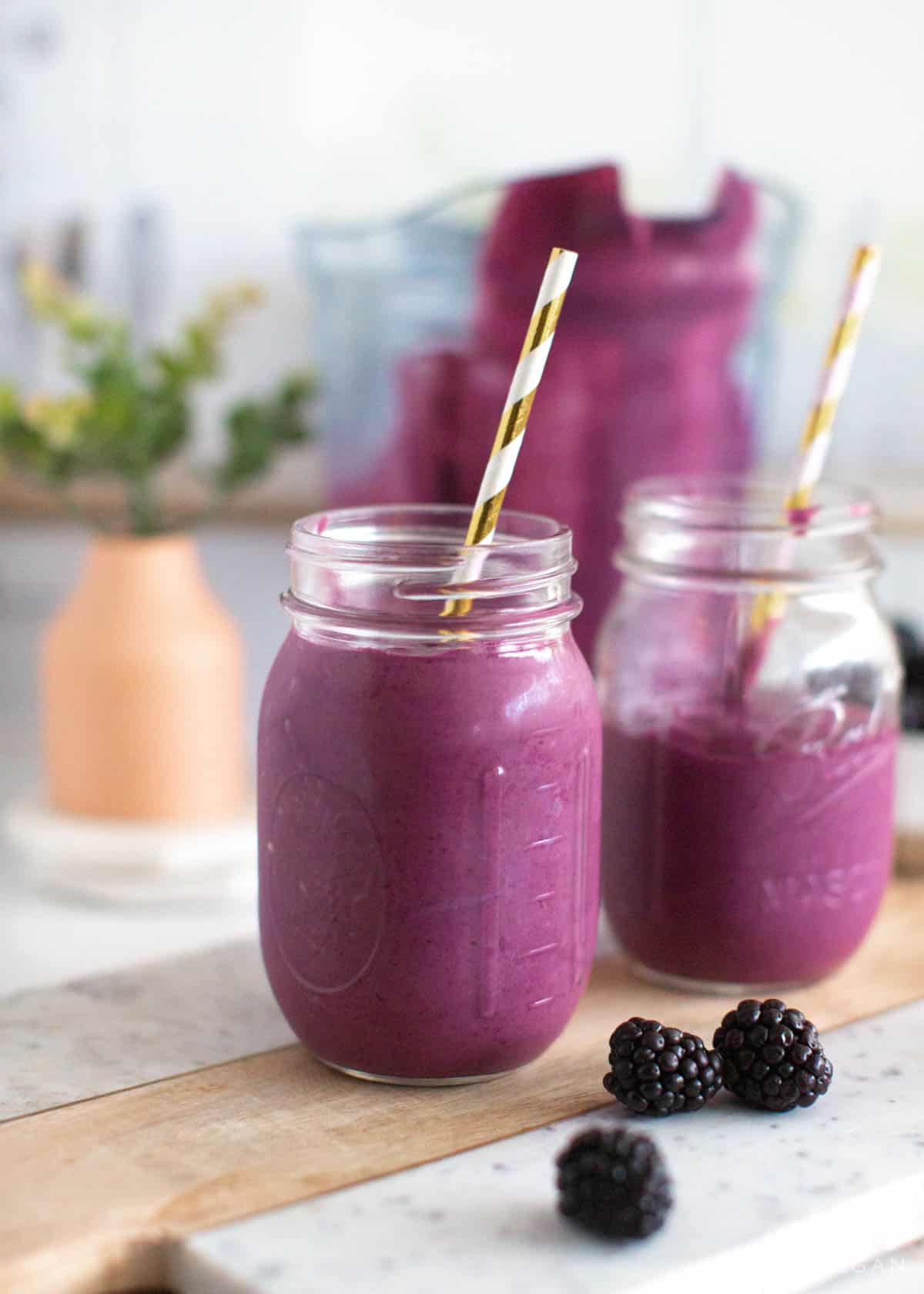 Two blackberry smoothies in mason jars with straws.