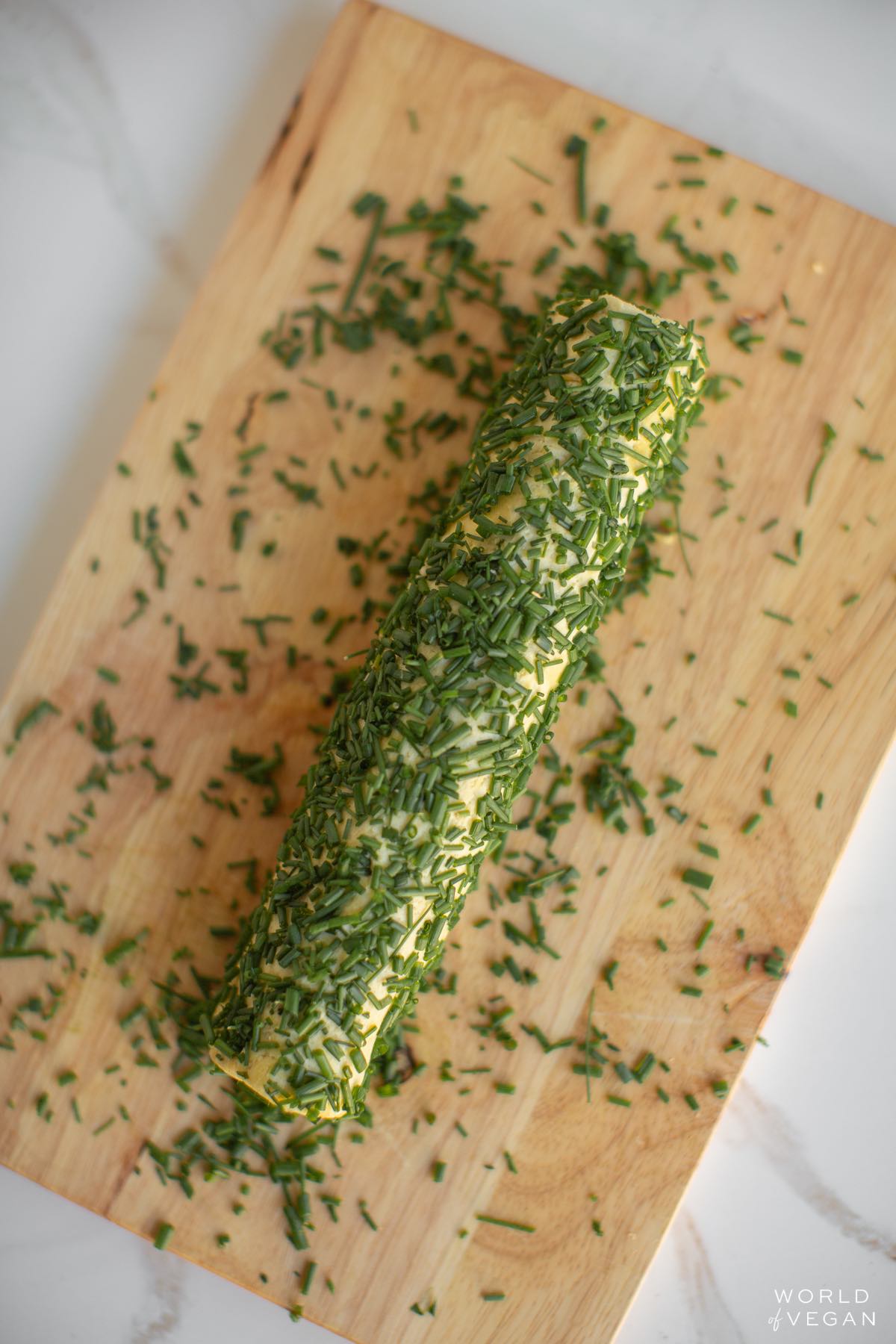 Rolling the vegan cheese log in chopped chives on a cutting board.