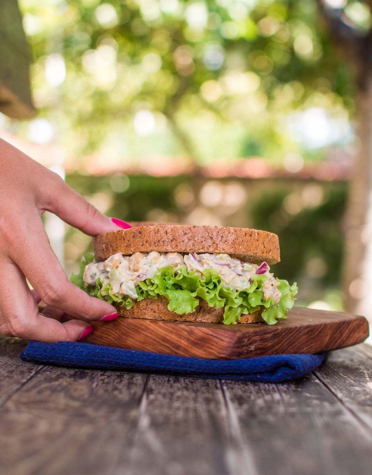 A hand reaching for a vegan chicken salad sandwich.