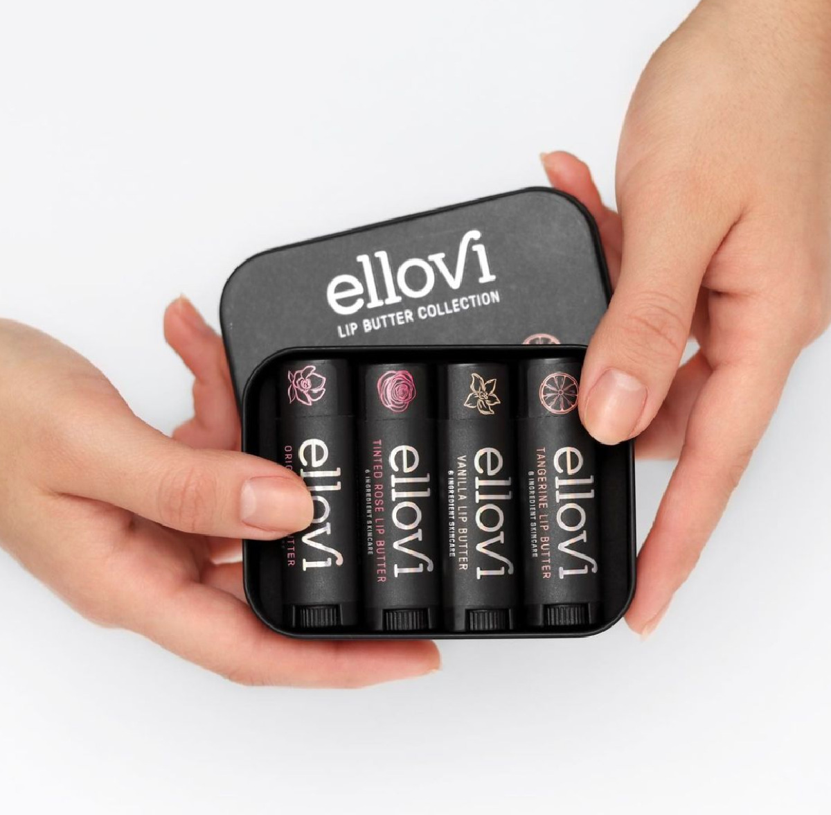 Two hands holding a black gift box of Ellovi Lip Butter Collection balms against a white background. 