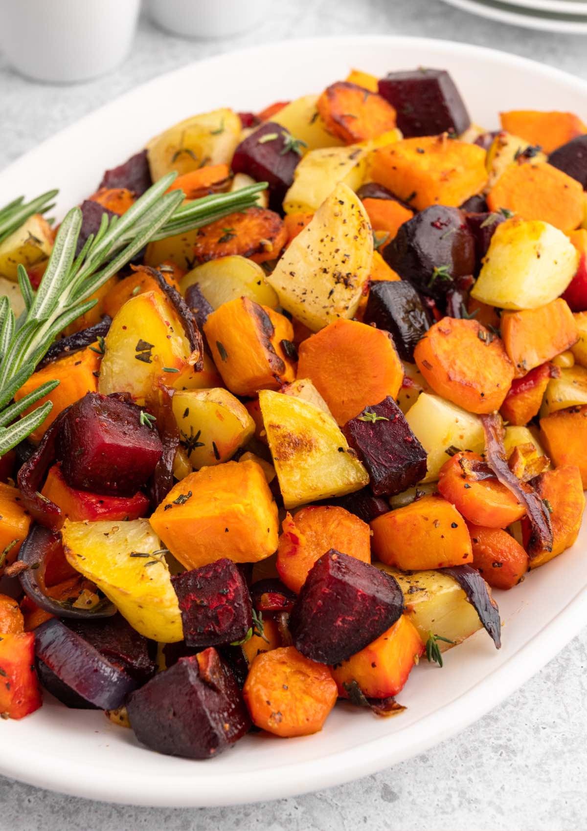 A large white serving platter with roasted fall vegetables on a holiday Thanksgiving table. 