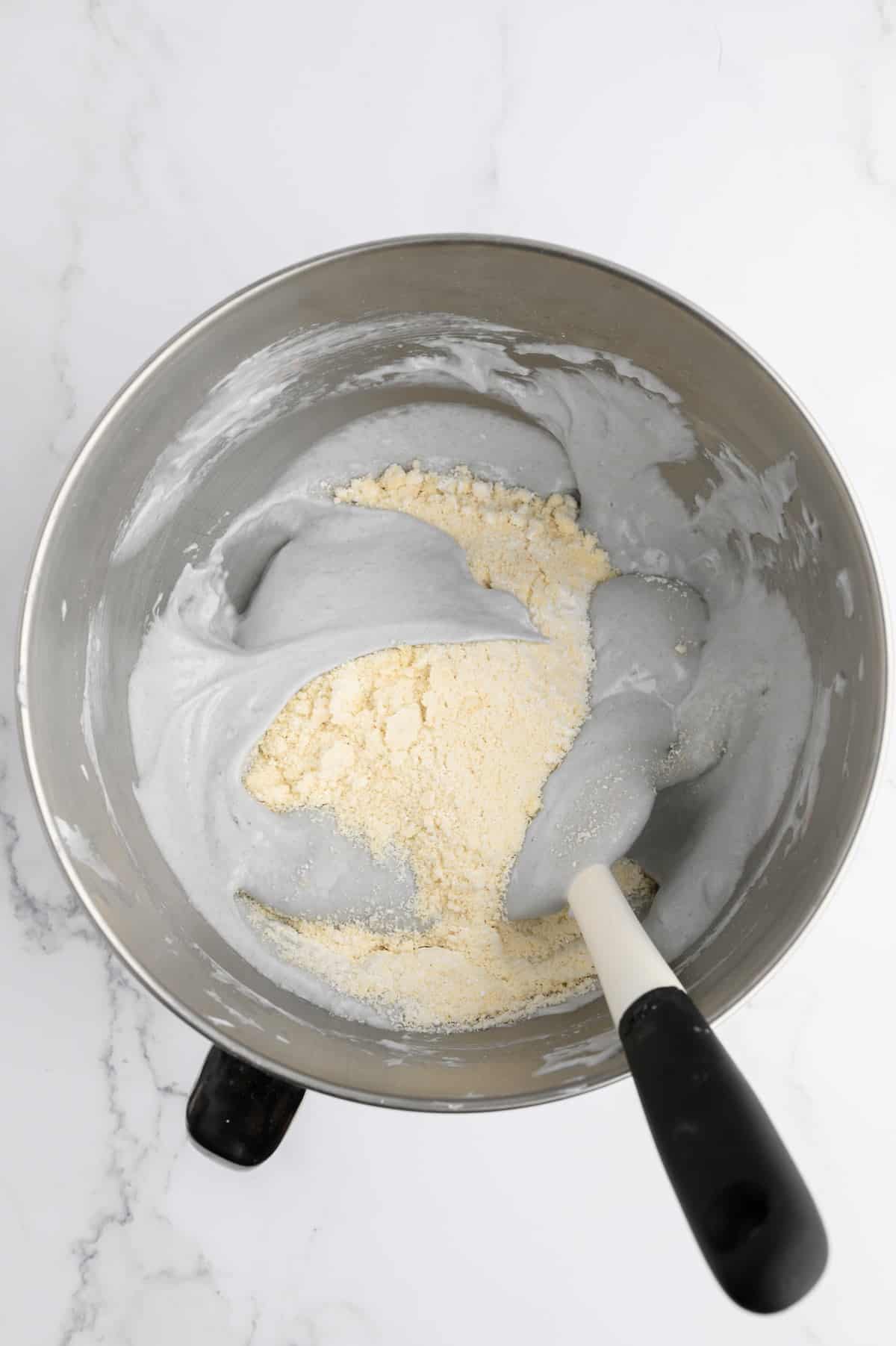 Folding the almond flour mixture into the aquafaba mixture with a rubber spatula.