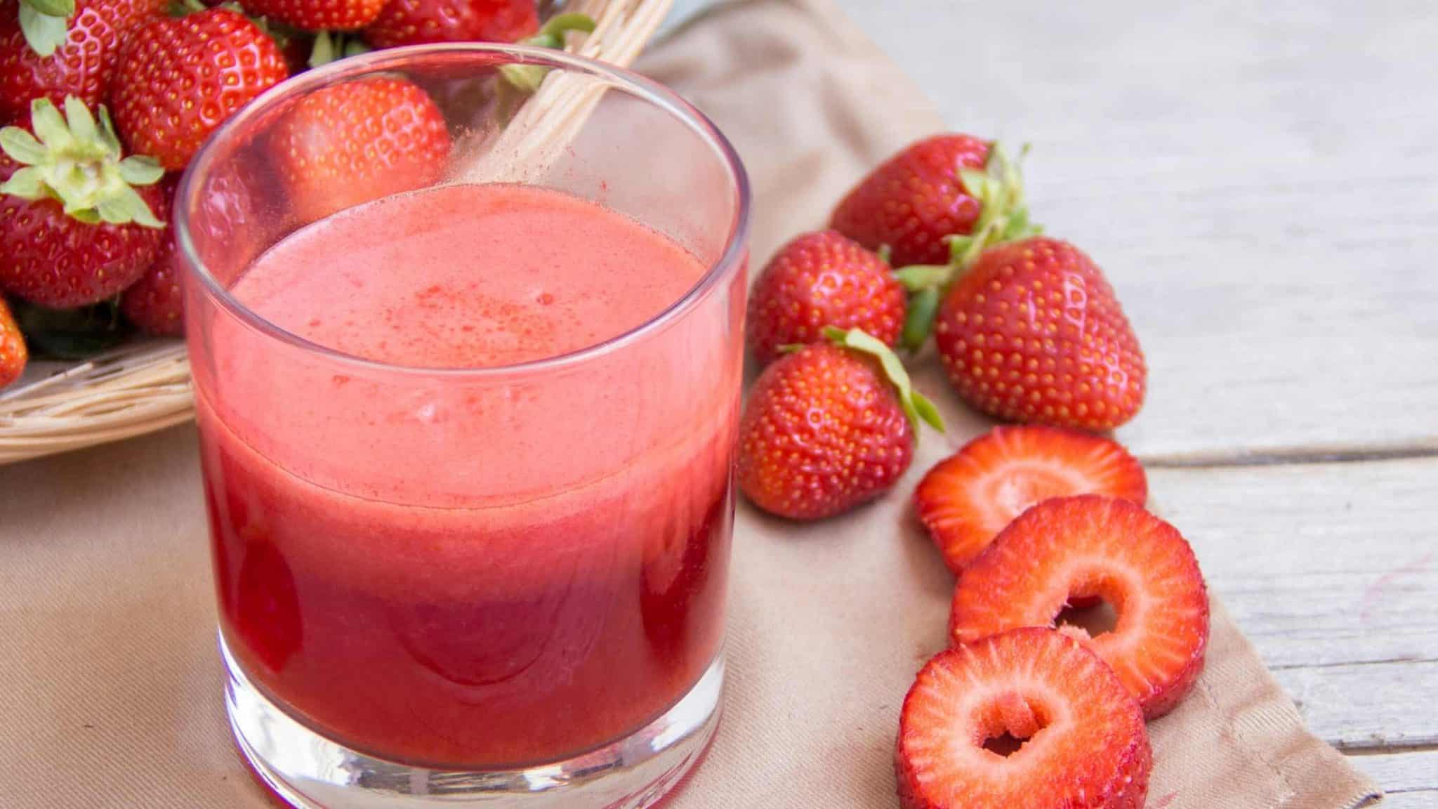 fresh strawberry juice served in a glass surrounded by ripe strawberries on a table
