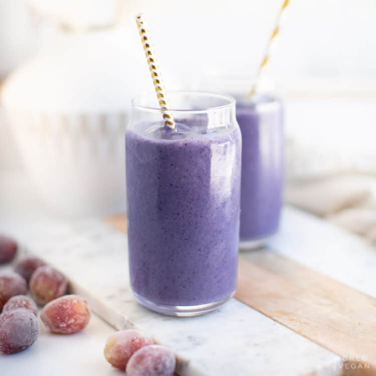 Two glasses filled with a grape smoothie and served with straws.