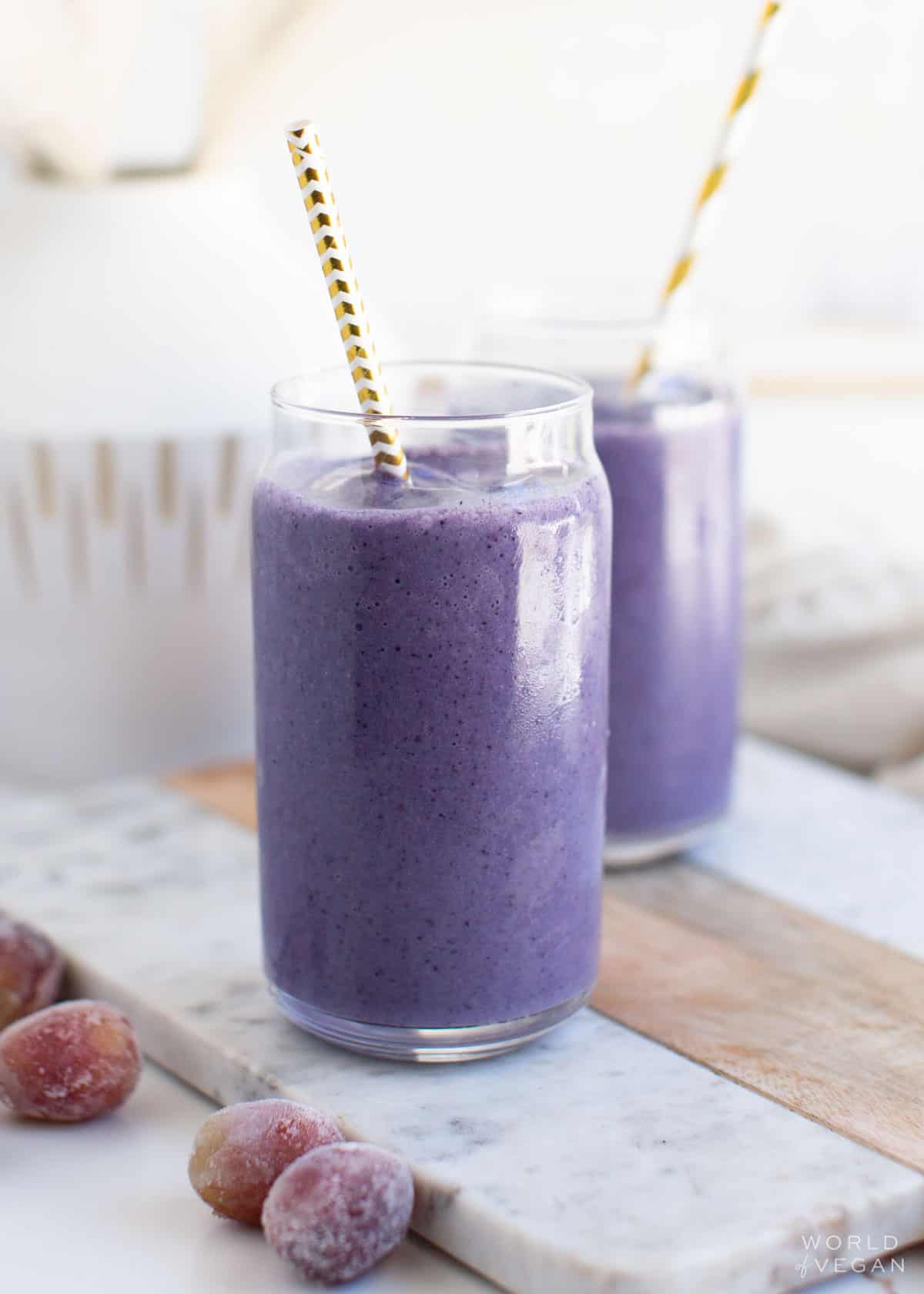 Two glasses filled with a purple grape smoothie next to frozen grapes.