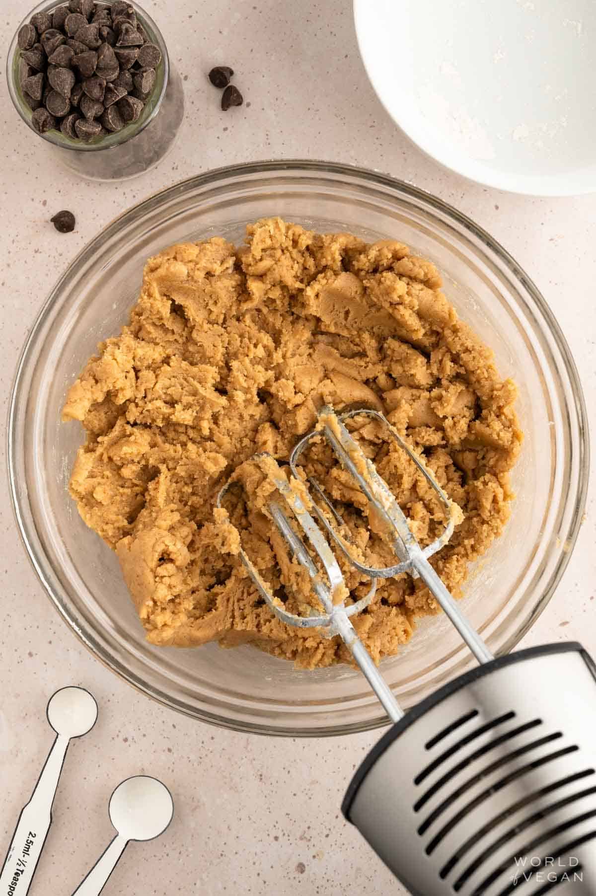 Making peanut butter cookie dough in a glass bowl with a hand mixer.