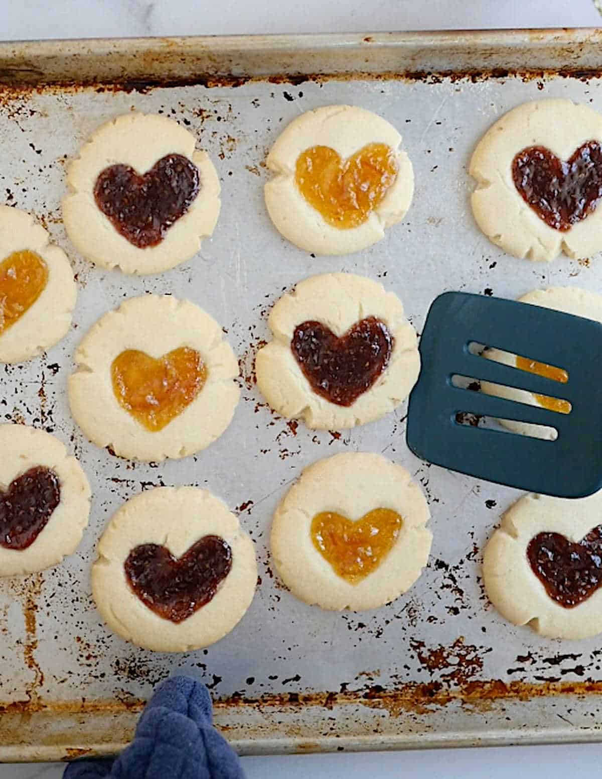 Baked vegan thumbprint cookies on a cookie sheet with a spatula.